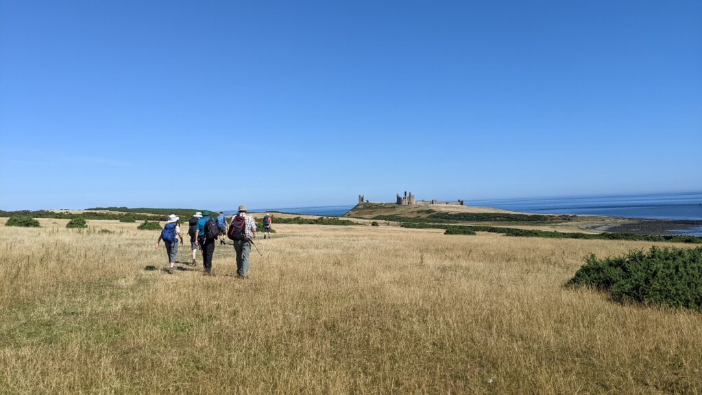A group walking along the coast towards Dunstanburgh Castle