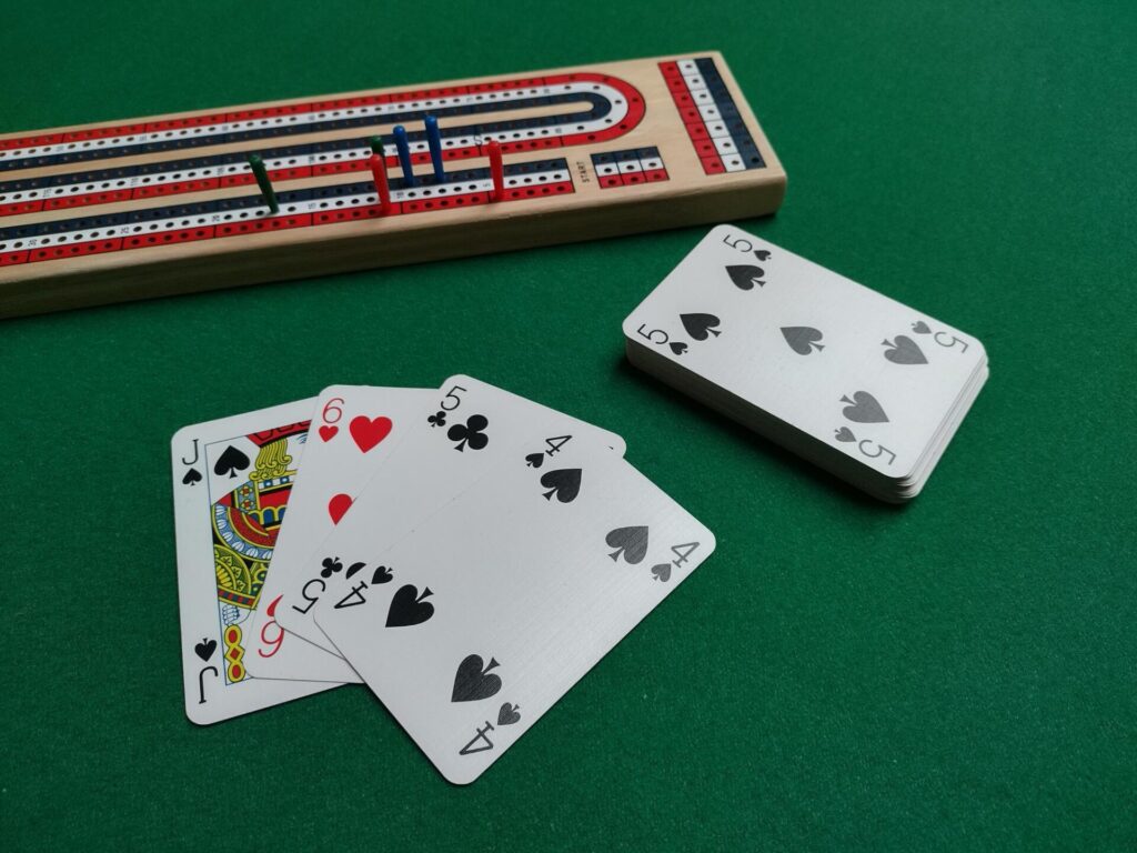 A cribbage board a pack of cards and hand of cards on a green beige table top.