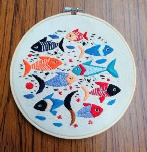A circular embroidered picture with nine fish in various sizes and colours
