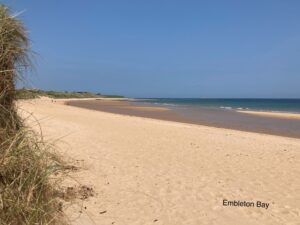 Taken from a low angle with yellow sand in the foreground stretching away in a curved bay towards a blue sea and sky
