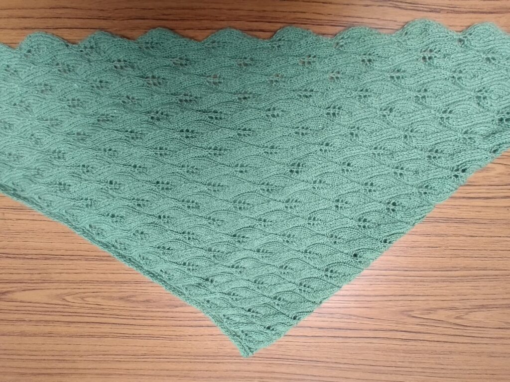 A green knitted shawl laid out on a table in a triangle shape